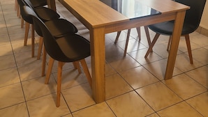 Una larga mesa de madera con sillas negras en una habitación con suelo de baldosas.