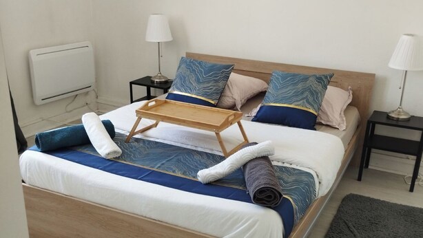 Una cama bien hecha con estructura de madera, una bandeja y toallas enrolladas.