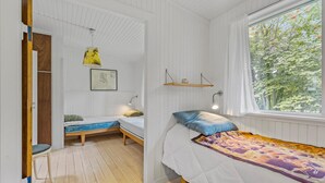 Ein Zimmer mit zwei Betten, Holzboden, einem Fenster mit Blick auf Bäume und einer Hängelampe.