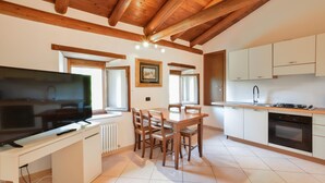 Una cocina moderna con armarios blancos, una mesa de comedor con sillas, un televisor de pantalla plana grande y un horno empotrado.