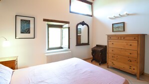 Un dormitorio con cama, cómoda, radiador, ventana y espejo.