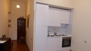 A compact kitchen with white cabinets, a stove, and a sink. There is a dining table with chairs in the adjacent room. - Suites in Rome 2 - Appartament (Rome)