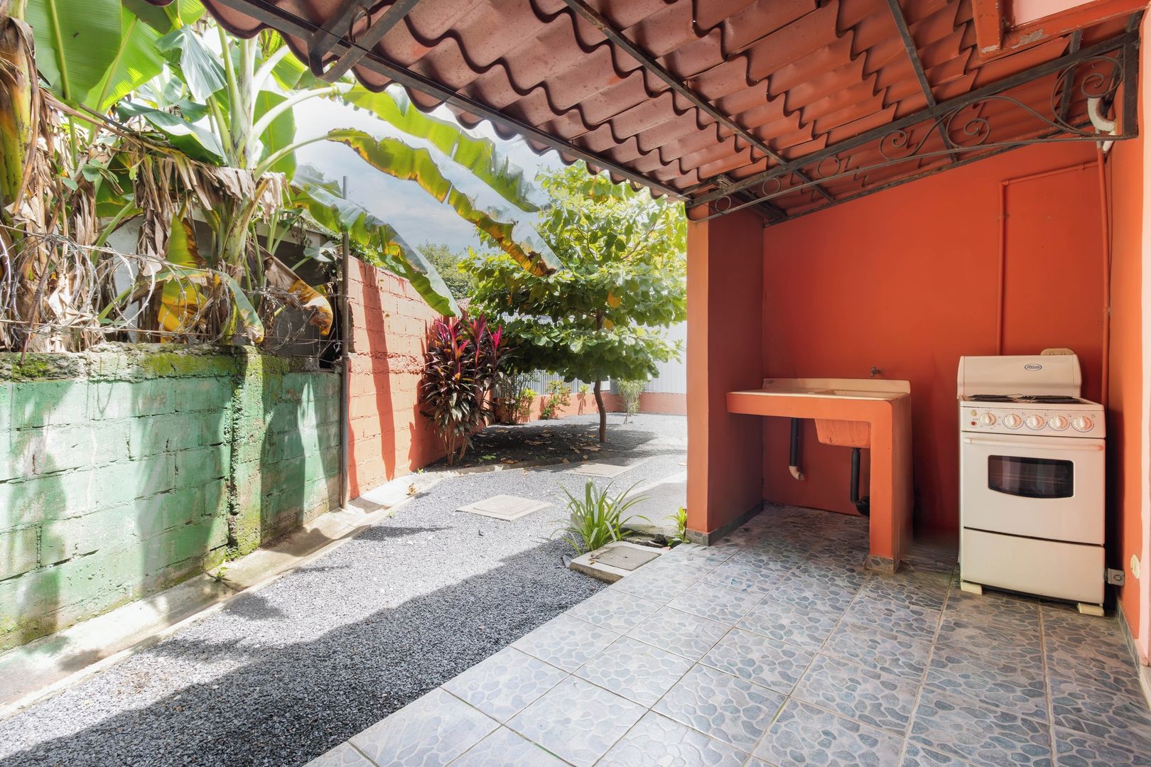 A covered outdoor area with a gas stove and oven, a table, and a green wall with plants.