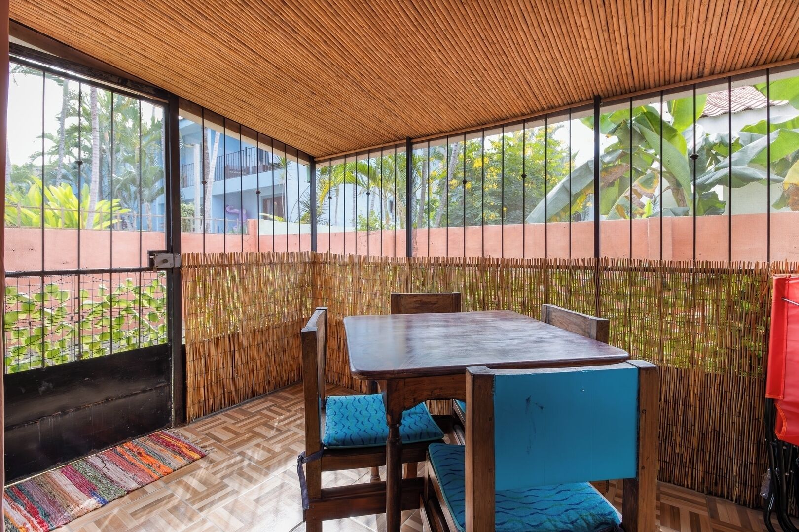 A room with a wooden ceiling, large windows, a bamboo wall, and a table with chairs.