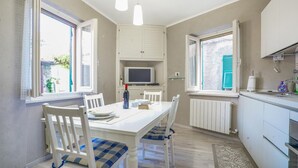Une cuisine compacte avec des meubles blancs, une table à manger avec des chaises, un téléviseur encastré et une fenêtre avec des volets.