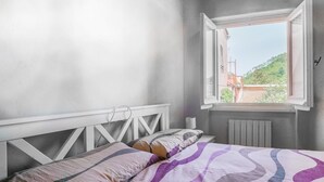 Une chambre avec un lit, une fenêtre dont le volet est ouvert, et une vue sur la verdure à l’extérieur.