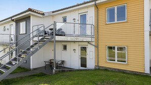 Un bâtiment à deux étages doté d’un balcon, d’un escalier et d’un petit espace extérieur aménagé pour s’asseoir.
