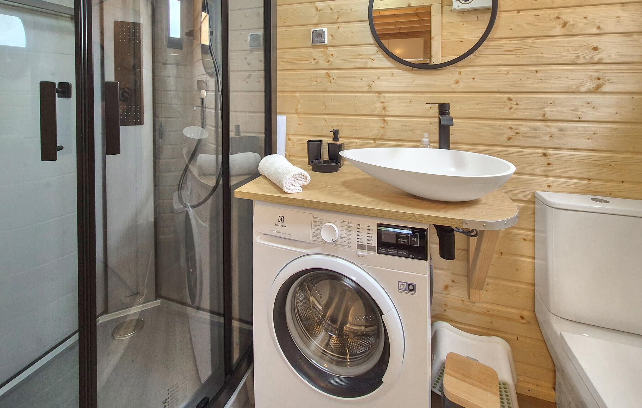 A compact, modern bathroom with a glass shower enclosure, a washing machine, and a sink with a wooden countertop.