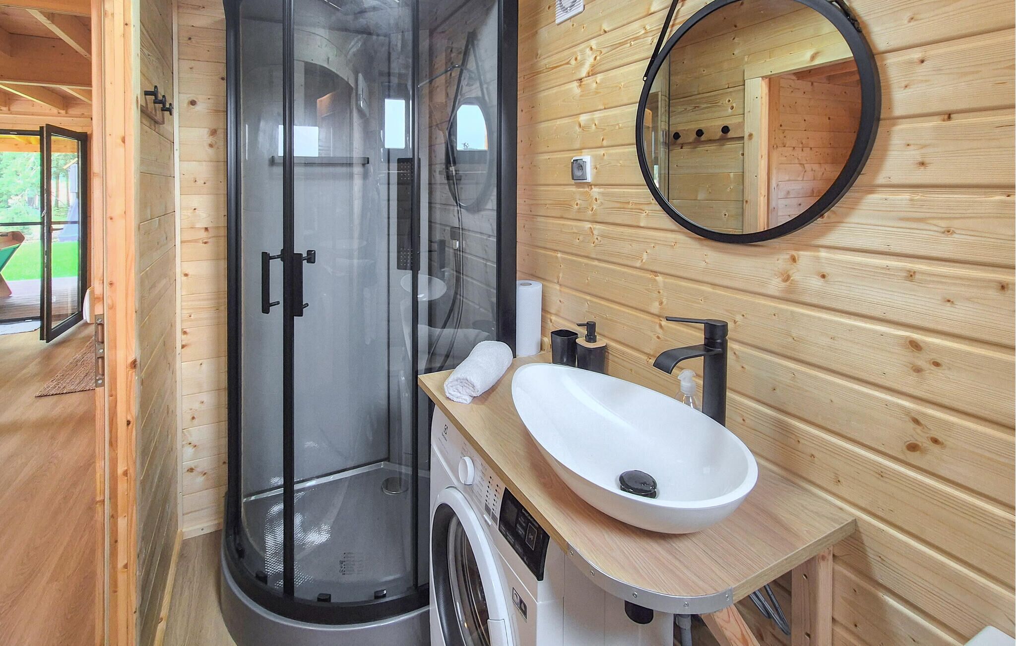 A wooden cabin bathroom with a glass-enclosed shower, a sink with a mirror, and a washing machine.