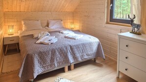 A cozy bedroom with a bed, bedside lamps, a dresser, and a window with a view of trees. - Nice home in Nowe Warpno with sauna (Nowe Warpno)