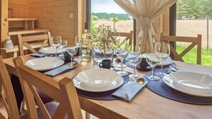 A wooden dining table set for four with white plates, clear glasses, and a vase with dried flowers. - Nice home in Nowe Warpno with sauna (Nowe Warpno)