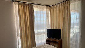 A hotel room with a bed, a TV on a wooden stand, and sheer curtains. - La Serena Avenida Del Mar 3 Bedrooms beach view  (La Serena)