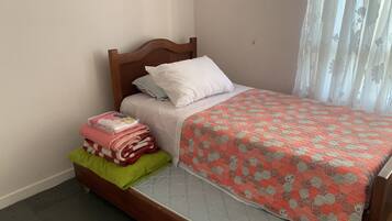 A single bed with a wooden headboard, a green pillow, and a pink blanket.