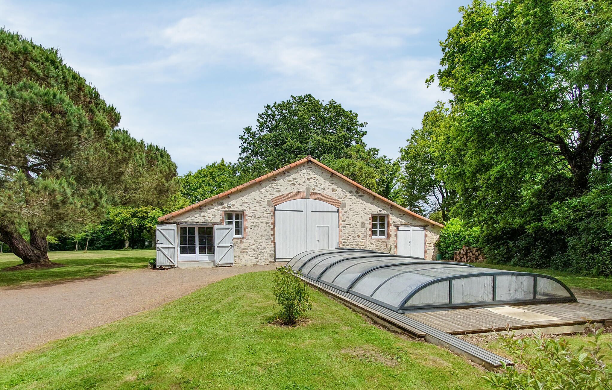 Un bâtiment en pierre doté d’une grande porte en arc de cercle, d’une petite structure adjacente avec une porte blanche, et d’une serre située à l’avant.