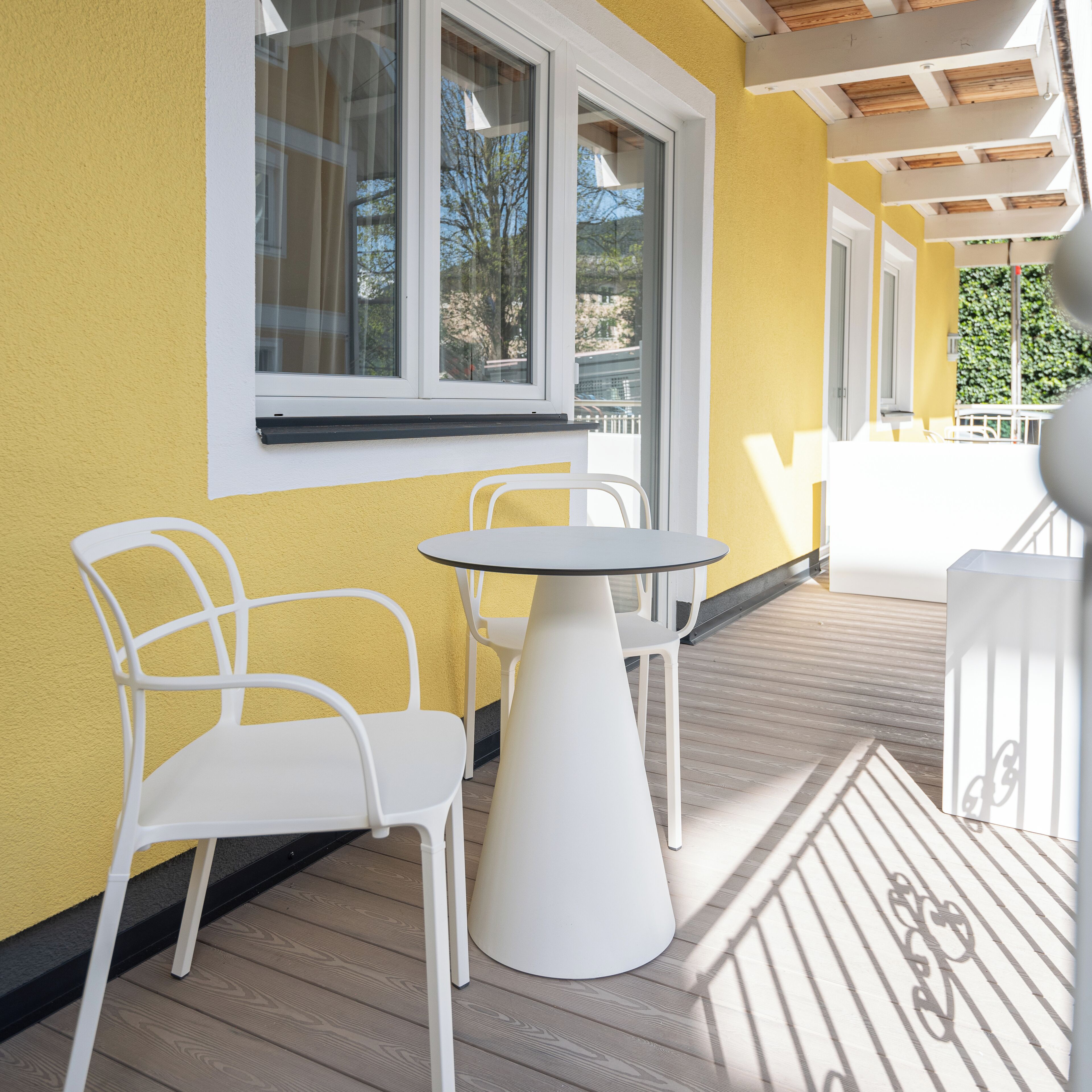 Eine Terrasse mit einer gelben Wand, weißen Stühlen und einem runden Tisch.