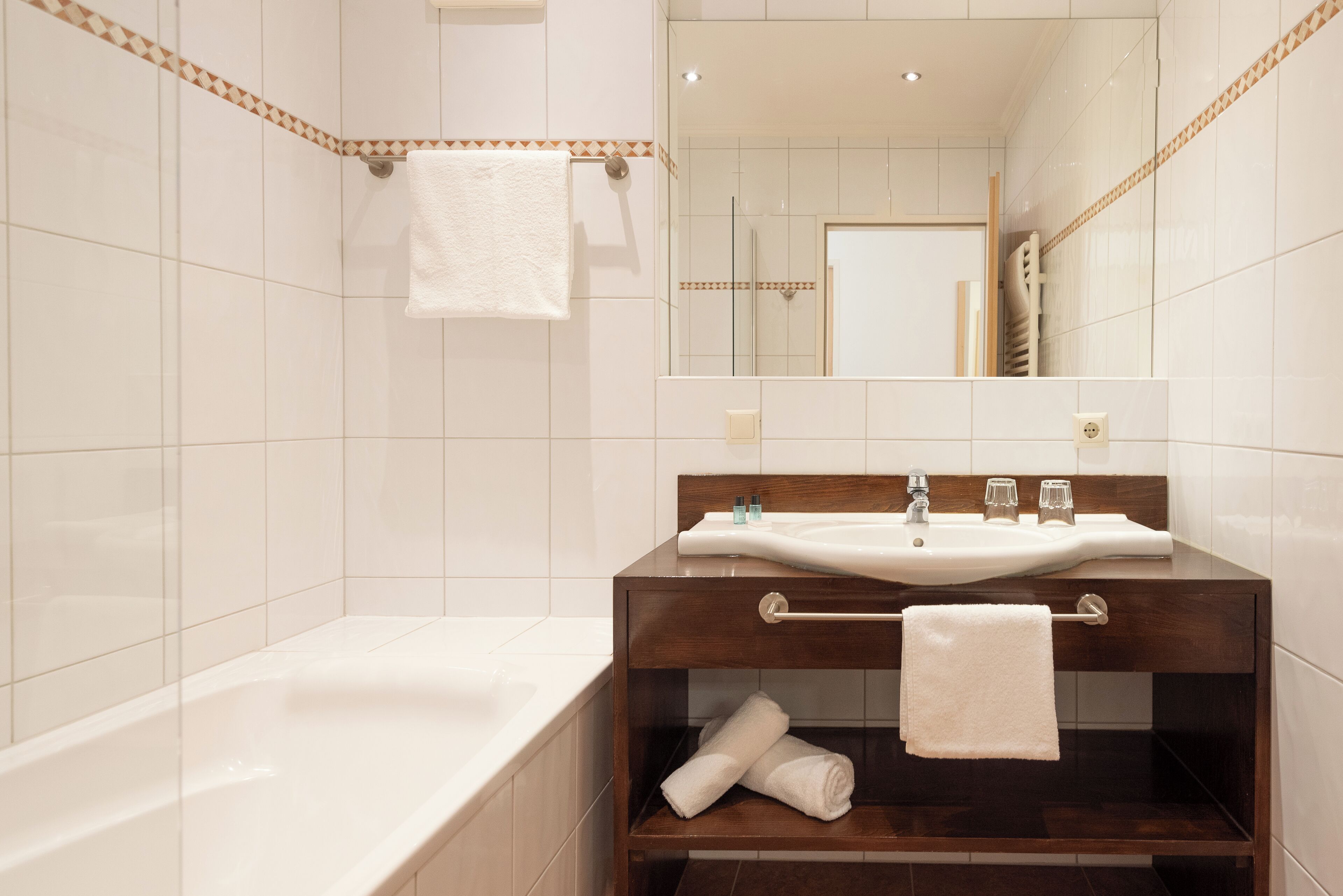 A modern bathroom with a bathtub, a wooden vanity with a sink, and a mirror.