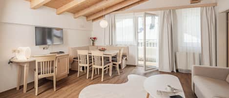 A modern living room with wooden beams, a flat-screen TV, a dining area, and a sofa.