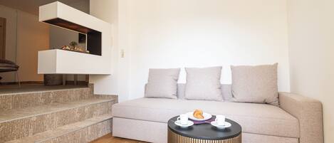 A modern living room with a beige sofa, a round black side table, and a staircase leading to an upper level.