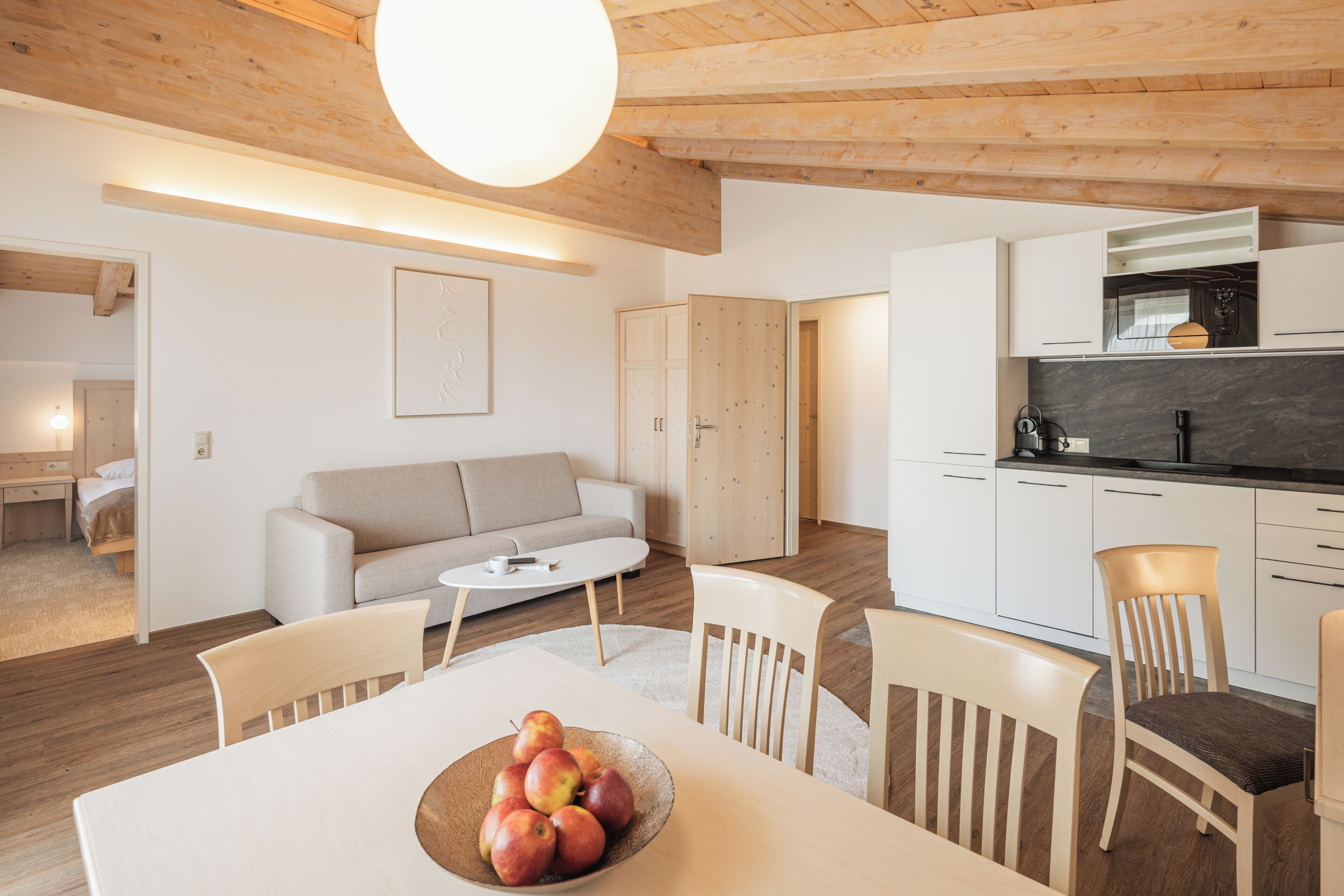Una cocina moderna con armarios blancos, techo de madera y un comedor con mesa y sillas.