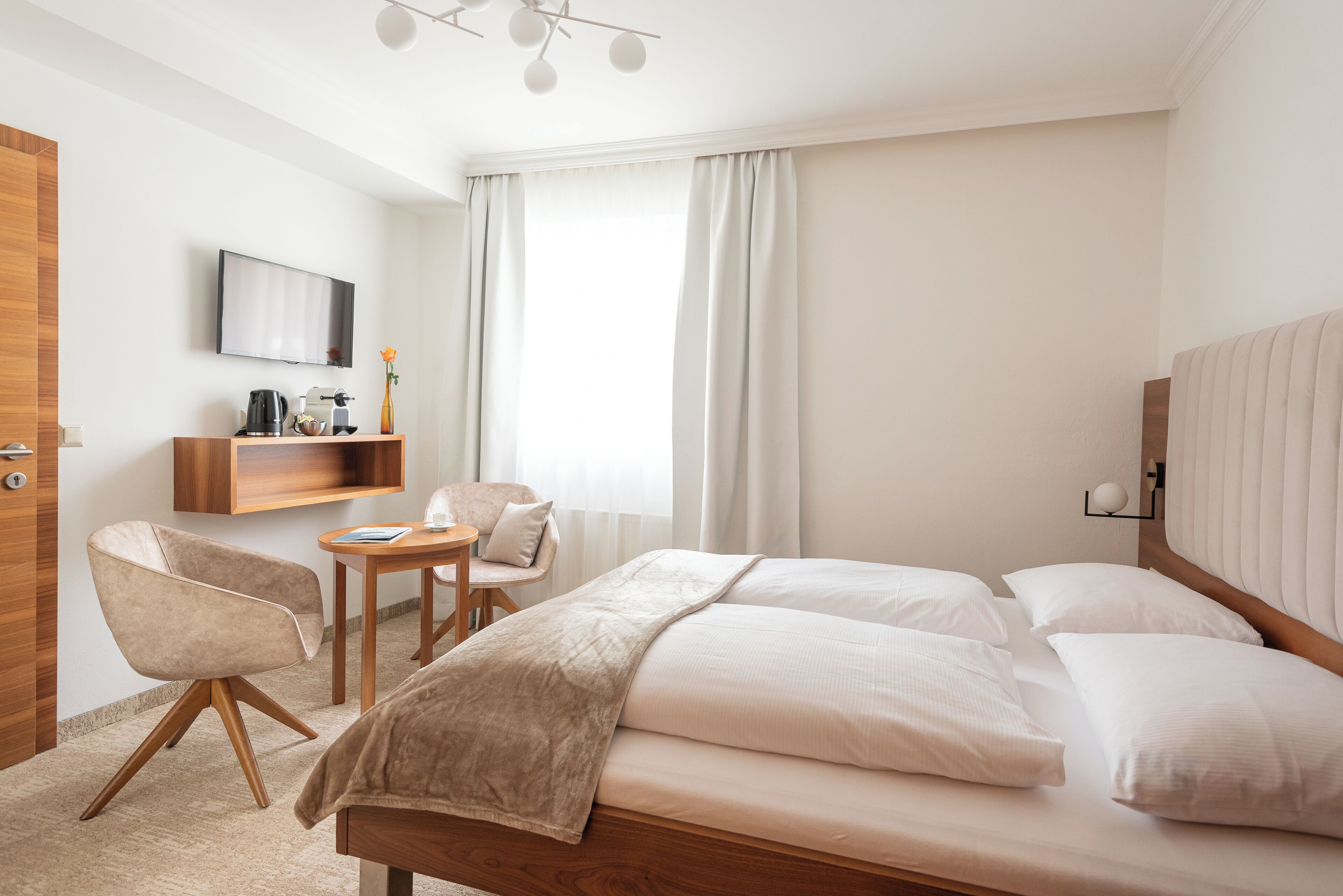 A hotel room with a bed, a desk, a chair, a TV, and a window with curtains.