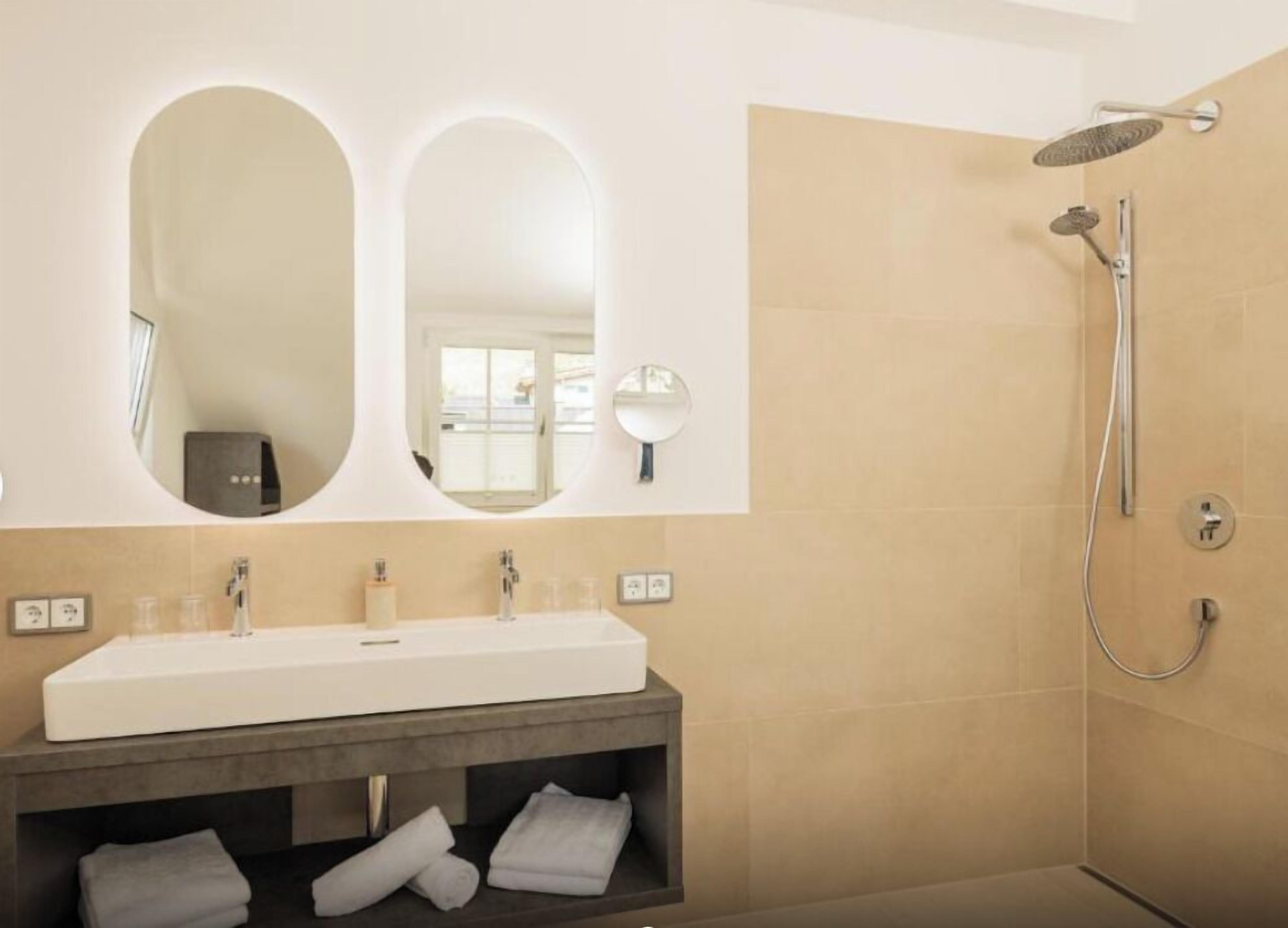 A modern bathroom with a large mirror, a shower, and a vanity with a sink and towel storage.