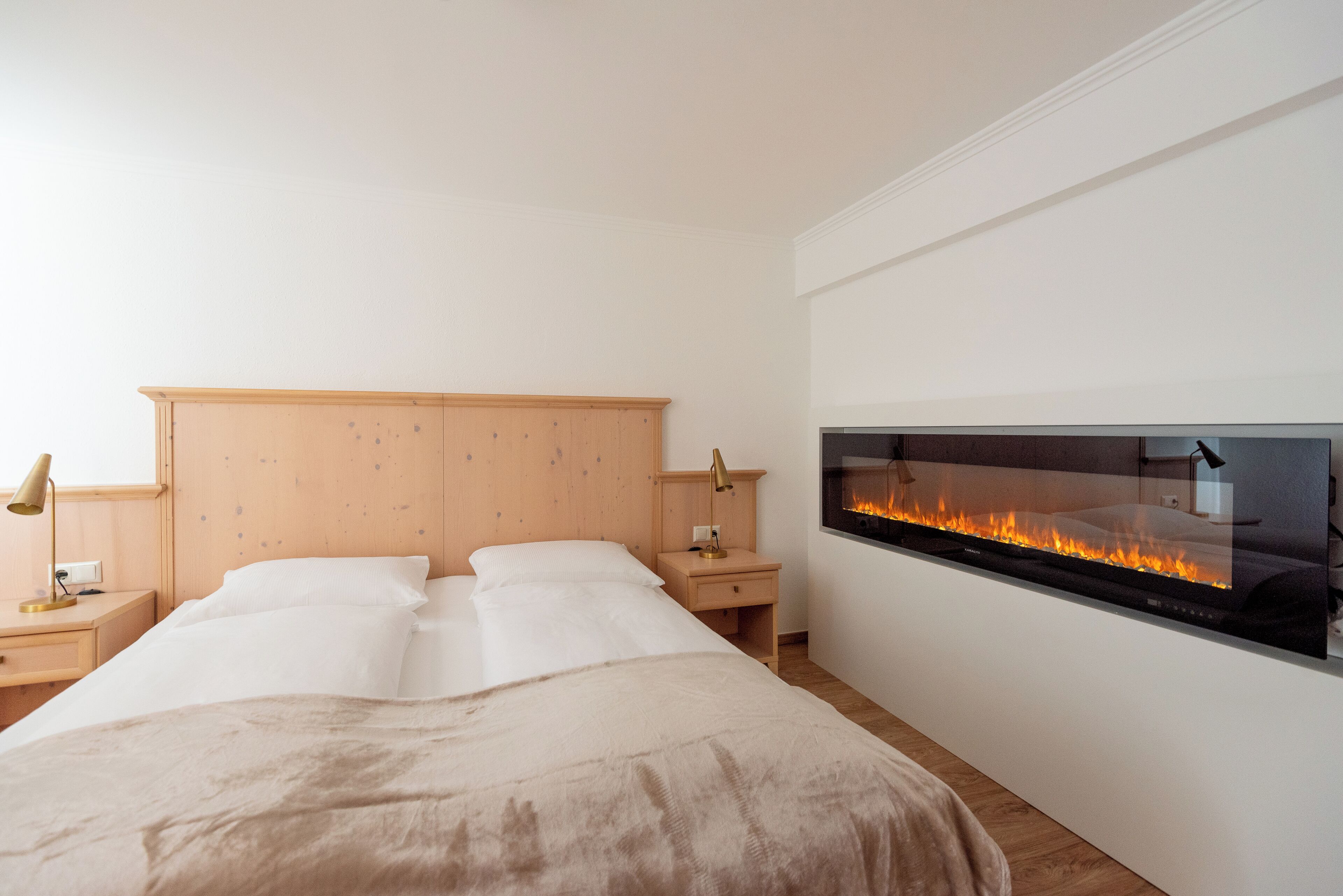 Quarto com cama, mesas de cabeceira, um aparador, lareira na parede e televisão.