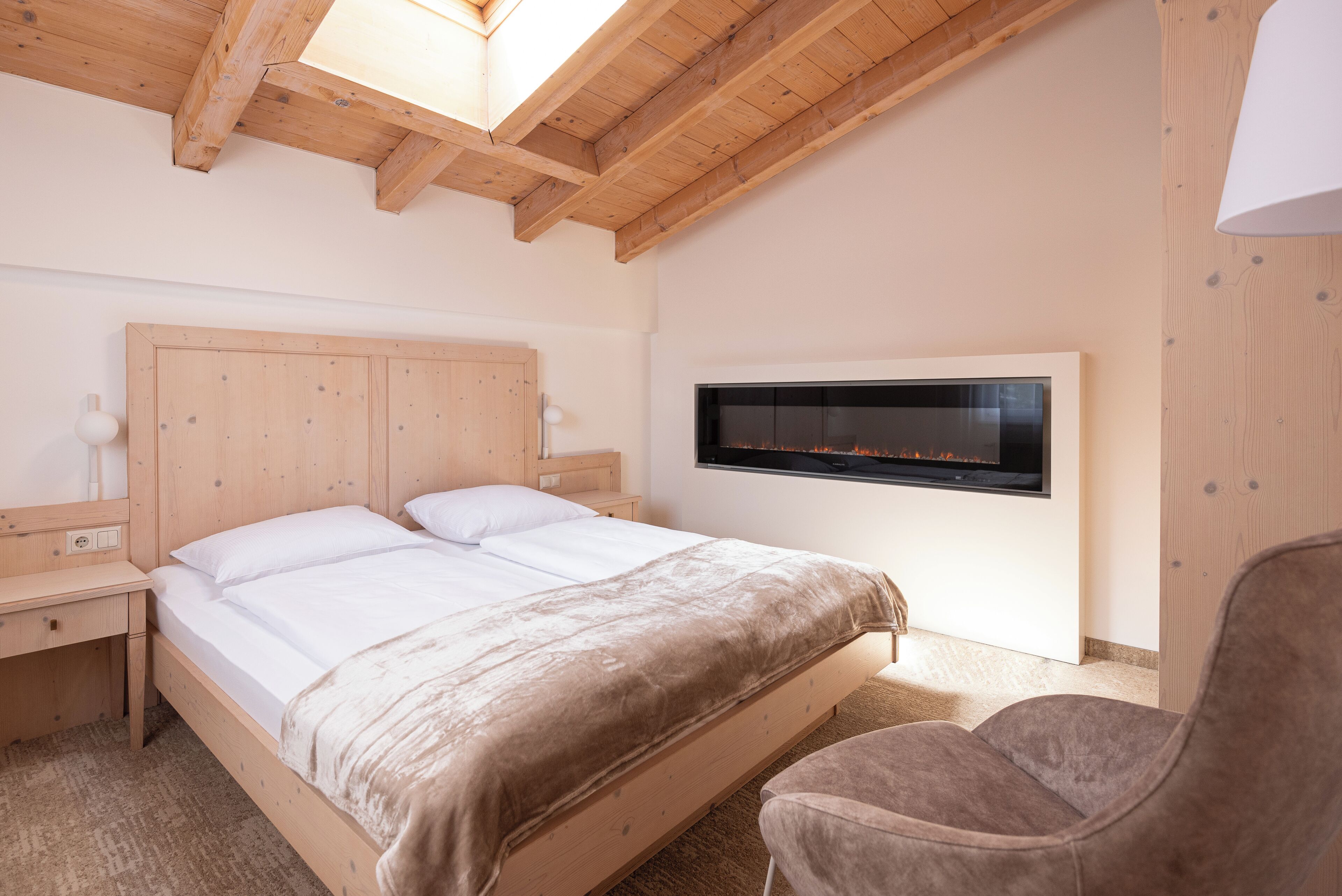 A bedroom with a wooden bed, a mounted TV, a nightstand, and a chair.