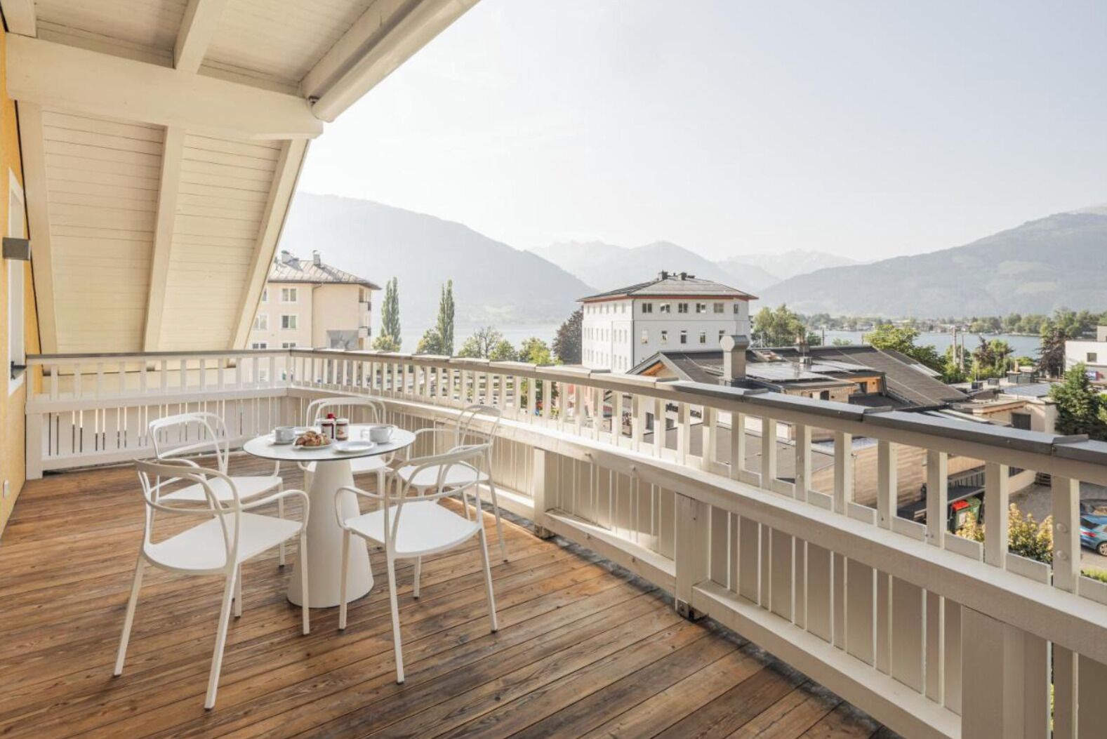 Eine Holzterrasse mit einem runden Tisch und Stühlen, mit Blick auf einen See und Berge.