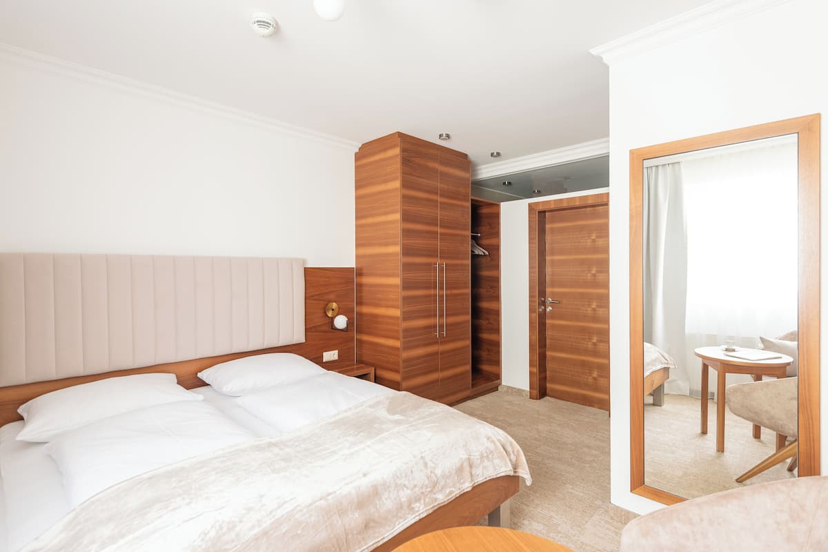 A hotel room with a large bed, wooden wardrobe, a small table, and a chair.