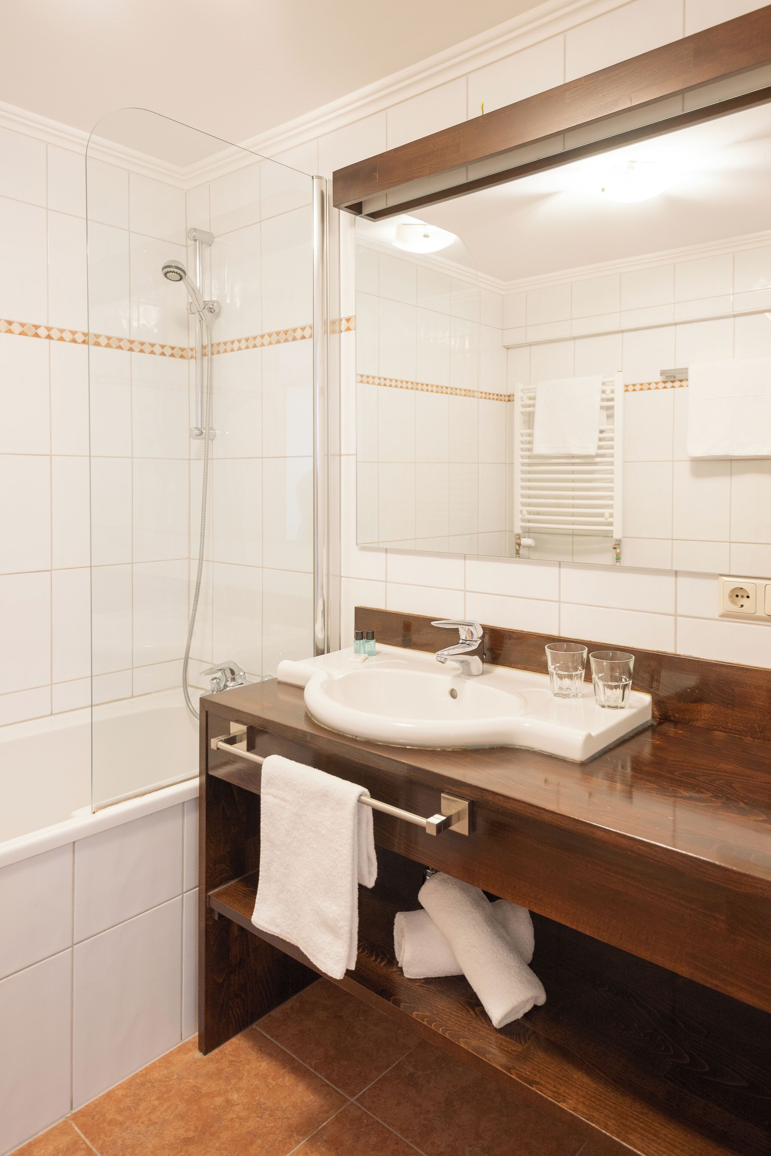 Un baño con ducha de vidrio, un lavamanos con espejo y un perchero con toallas.