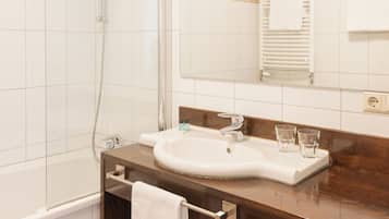 Un baño con ducha de vidrio, un lavamanos con espejo y un perchero con toallas.