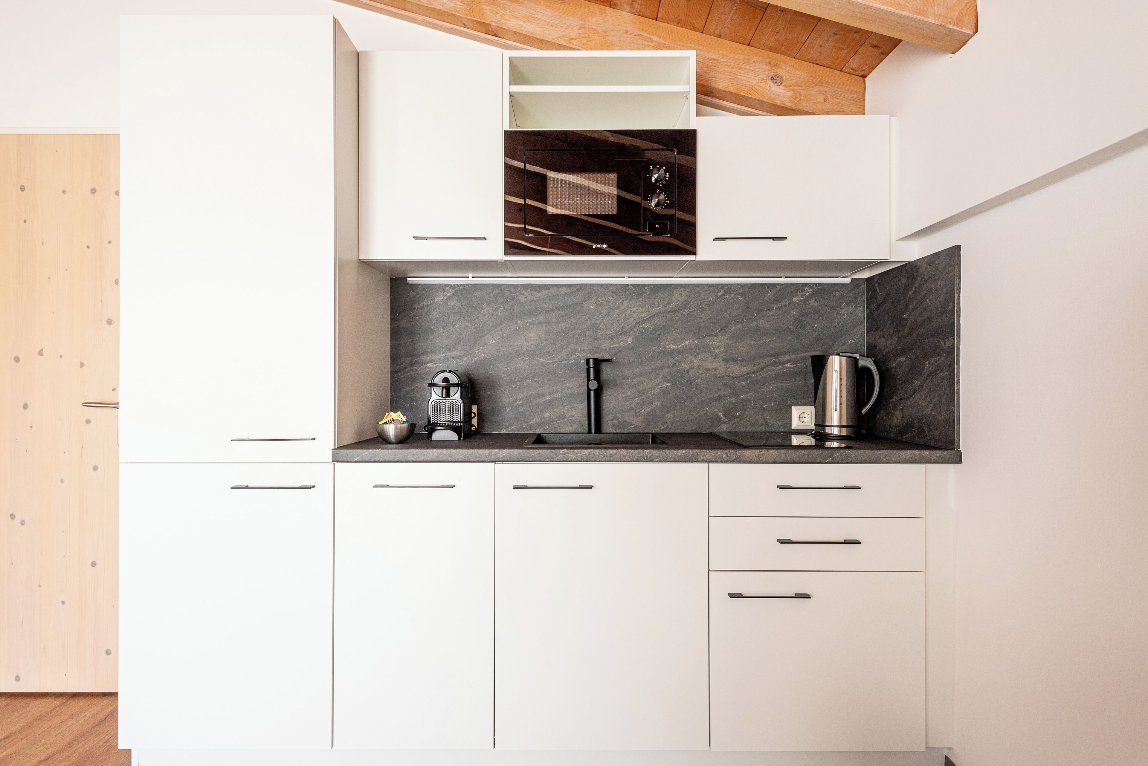 A modern kitchen with white cabinetry, a black countertop, and a built-in oven.