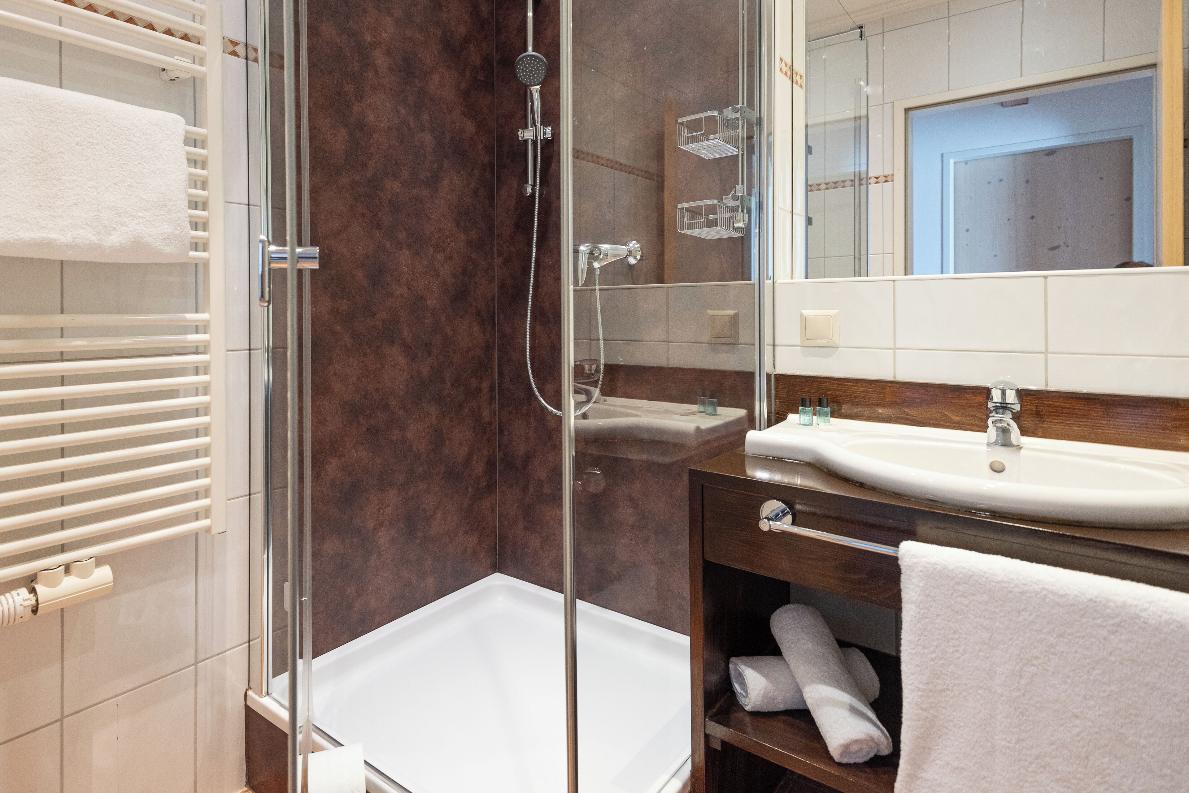 A modern bathroom with a glass-enclosed shower, a white bathtub, and a vanity with a sink and mirror.