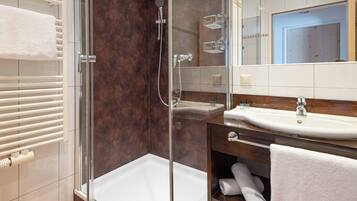 A modern bathroom with a glass-enclosed shower, a white bathtub, and a vanity with a sink and mirror.