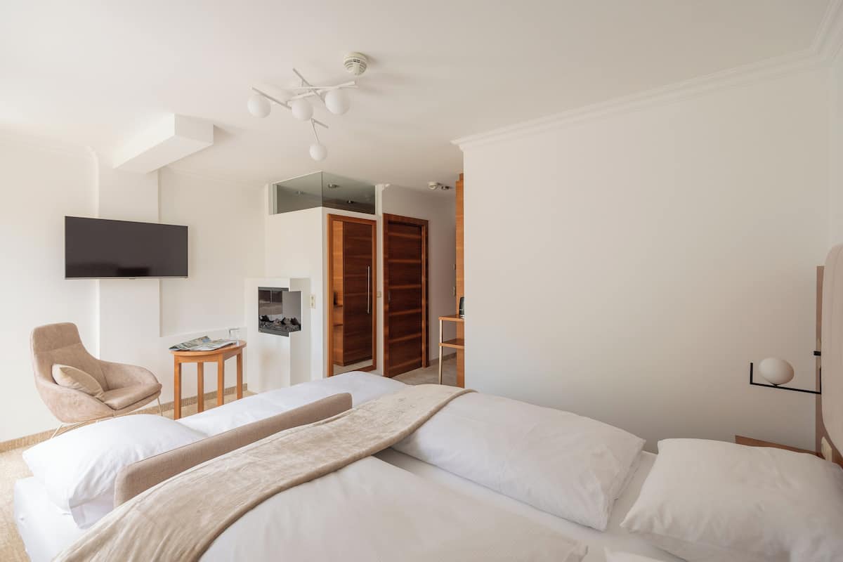 A modern hotel room with a large bed, a TV mounted on the wall, a wooden wardrobe, and a small side table.