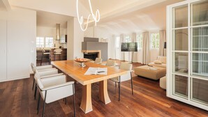 A spacious living room with a wooden dining table, white leather chairs, a sofa, and a large sliding glass door. - das zellersee (Zell am See)
