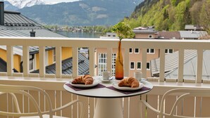 A balcony with a table set for two, two croissants, two cups, and a vase with a plant. - das zellersee (Zell am See)