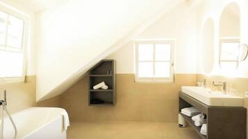A modern bathroom with a bathtub, a vanity with a mirror, and a shelf with towels.