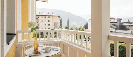 A balcony with a round table, chairs, and a vase of flowers.
