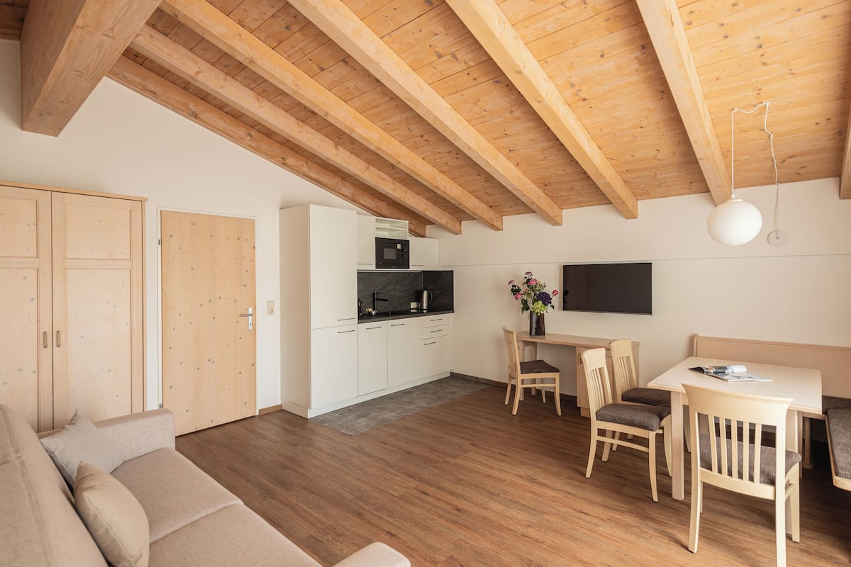 A modern kitchen with wooden beams, a dining area with a table and chairs, and a sofa in a living area.