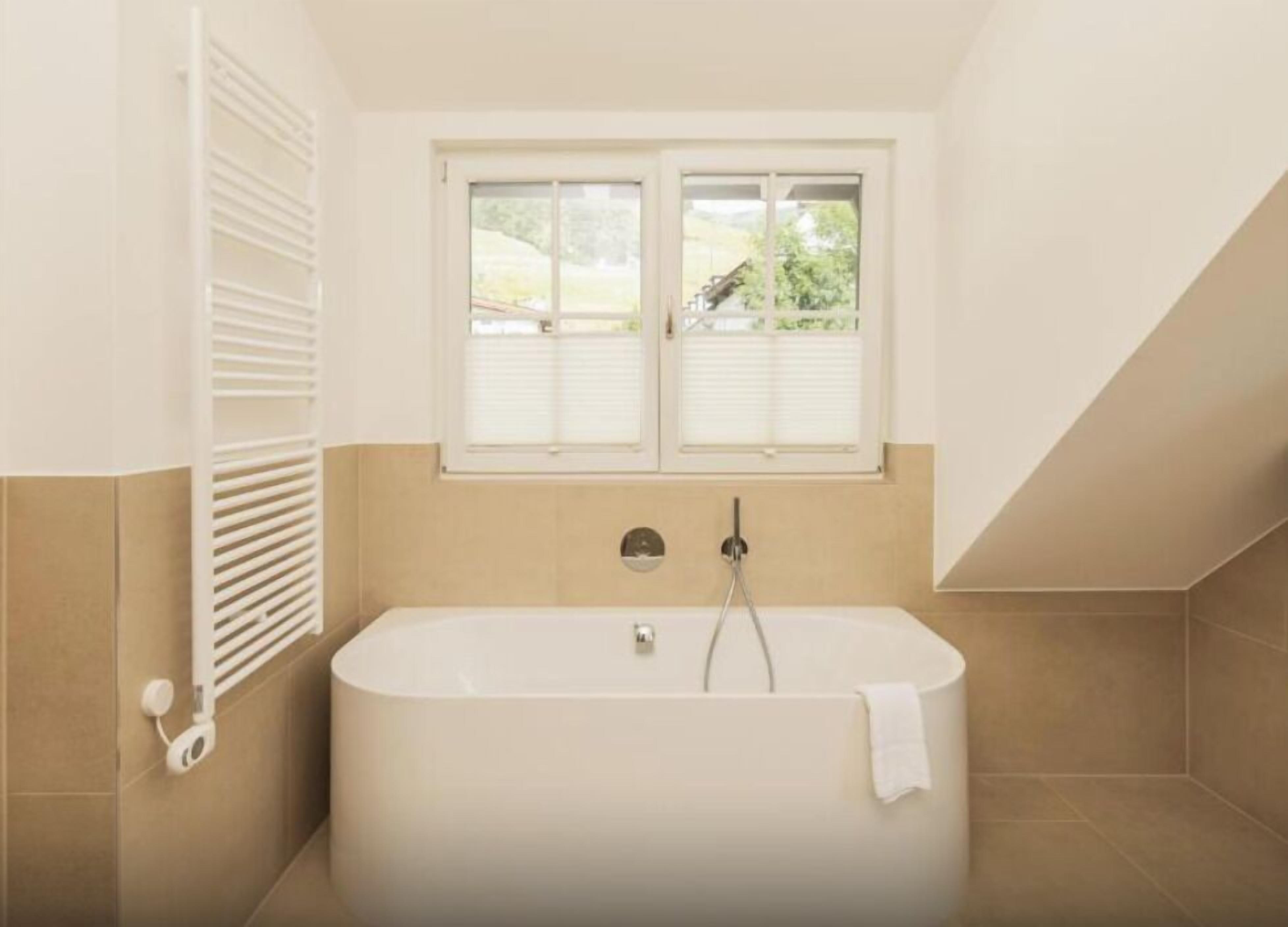 A modern bathroom with a freestanding bathtub, a window with shutters, and a towel hanging on the tub.