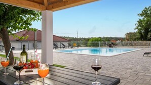 Ein Poolbereich mit einer Holzpergola, Liegestühlen und einem Tisch mit Getränken und einer Flasche.