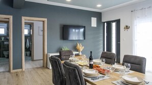 Ein Essbereich mit einem Holztisch, gedeckt für sechs Personen, umgeben von Stühlen. Ein Flachbildfernseher ist an der Wand über dem Tisch angebracht.
