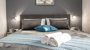 Ein ordentlich bezogenes Bett mit einer gestreiften Tagesdecke, zwei Kissen und einem aufgerollten Handtuch.
