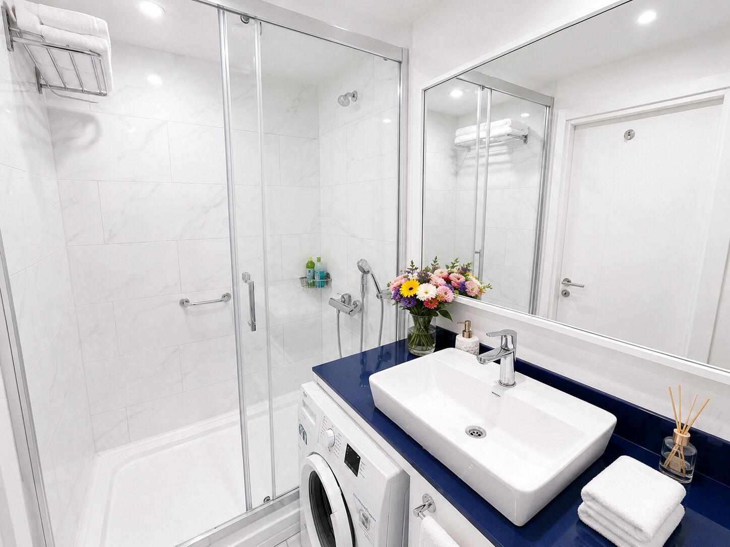 Une salle de bain moderne avec une douche à parois de verre, un lave-linge encastré, un grand lavabo et un miroir.