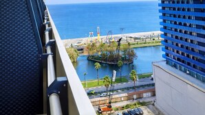 A view from a balcony overlooking a body of water, a beach, and a modern building with a blue facade. - Orbi City Sea View (Batumi)