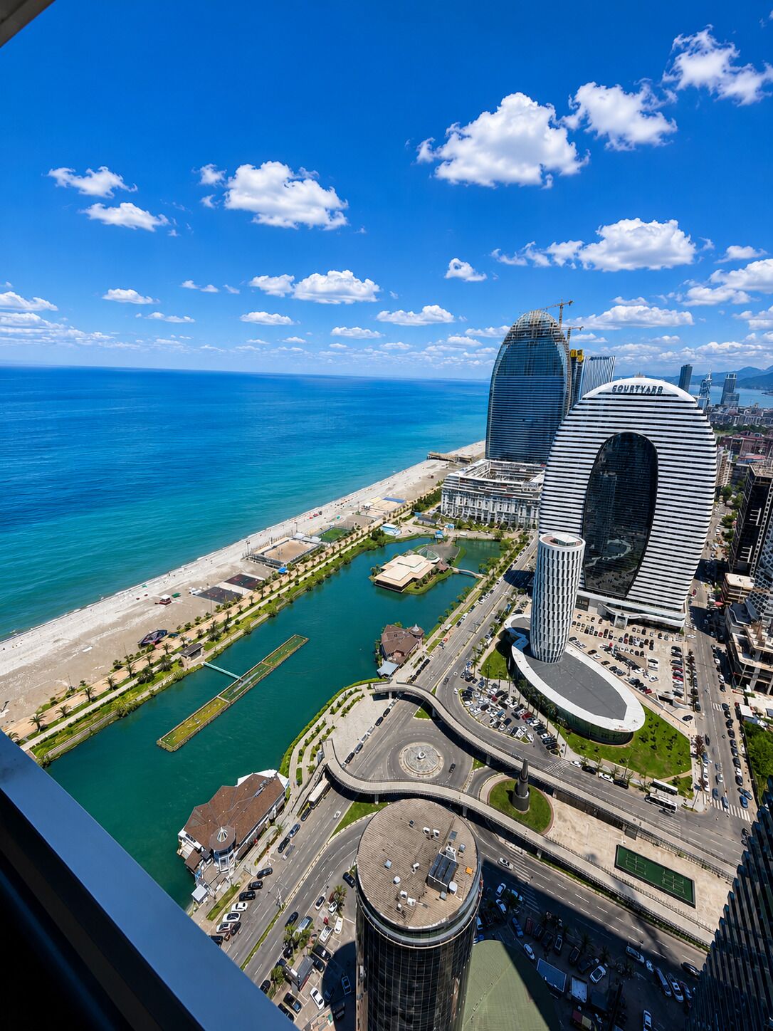 A coastal cityscape with modern architecture, a marina, and a clear blue sky.