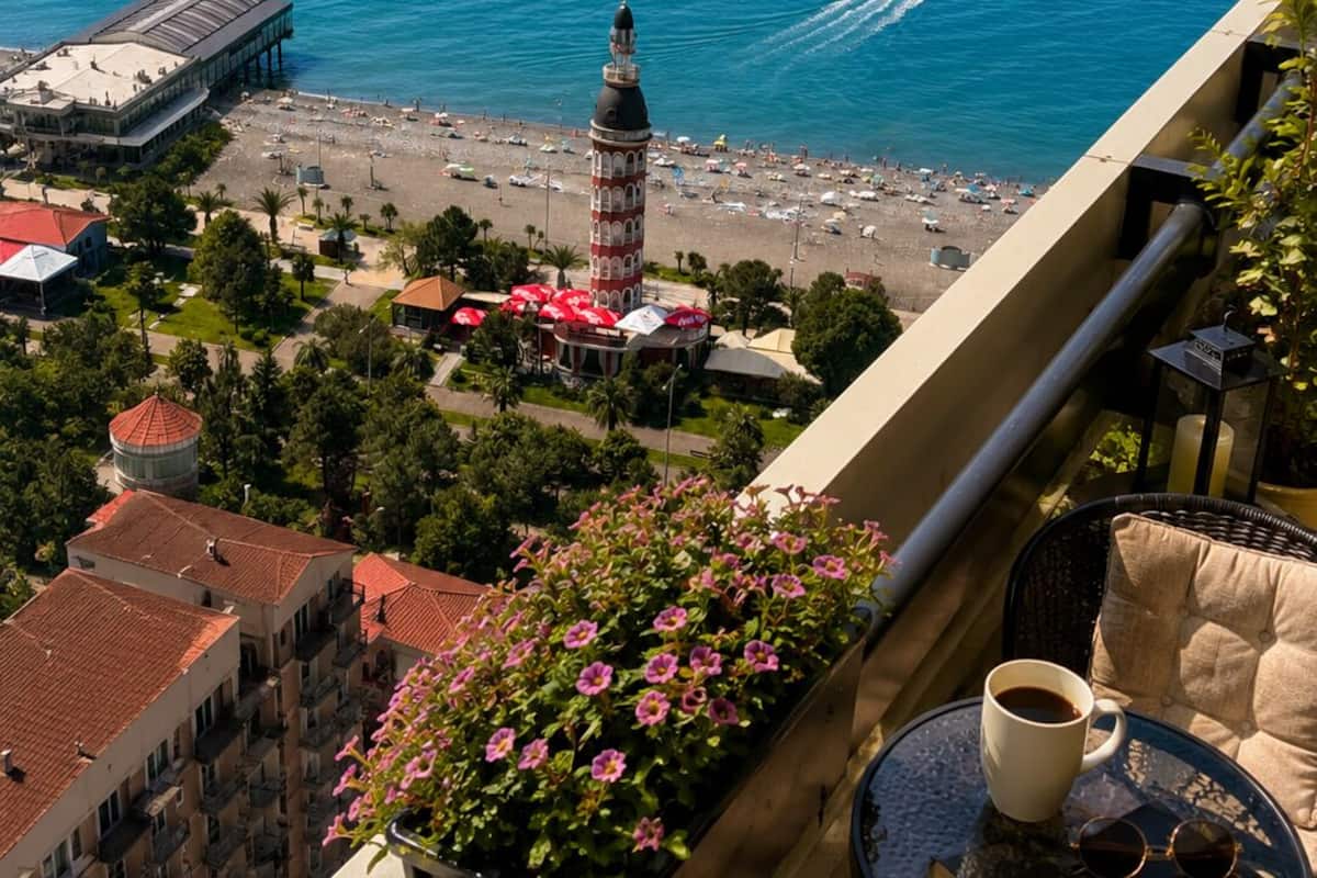 Un balcon avec vue sur la mer, un phare et une plage parsemée de parasols.