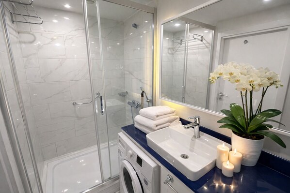 A modern bathroom with a glass shower enclosure, a white sink, a mirror, and a potted orchid. - Orbi City Sea View (Batumi)