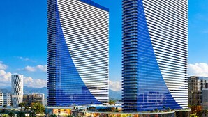 Two tall twin-tower buildings with a distinctive blue and white facade, surrounded by a modern urban environment with palm trees and a busy street. - Orbi City Sea View (Batumi)